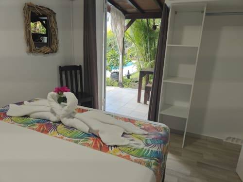 Tropical bedroom at Gites Kaladja with colorful bed runner, white towel swan, mirror, and pool view door in Port-Louis,
