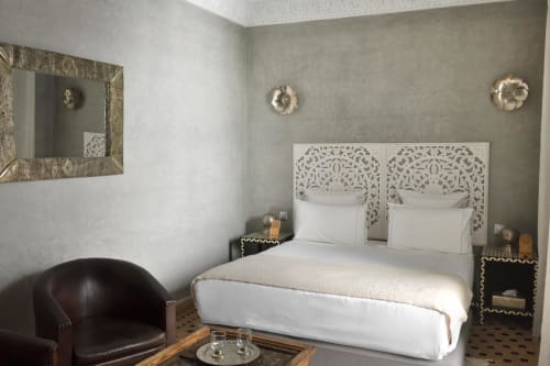 Elegante slaapkamer in Riad Palau Marrakech met verfraaide wit hoofdbord, donkere lederen stoel, gouden wandlampen en ingelijste spiegel