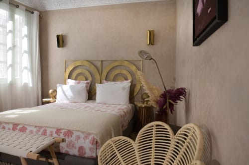 Luxe slaapkamer in Riad Palau Marrakech met gouden hoofdeinde, roze bloemenprint beddengoed, rieten stoel en moderne voorzieningen