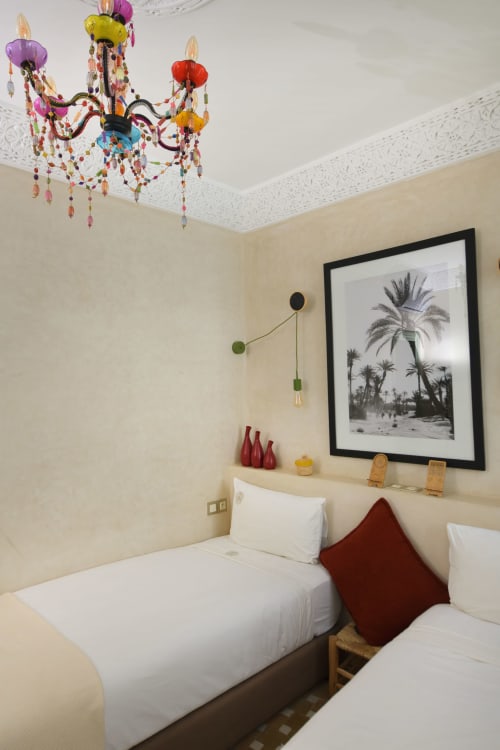 Boutiquehotelkamer in Riad Palau Marrakech met kleurrijke kroonluchter, witte beddengoed en palmboom kunstwerk