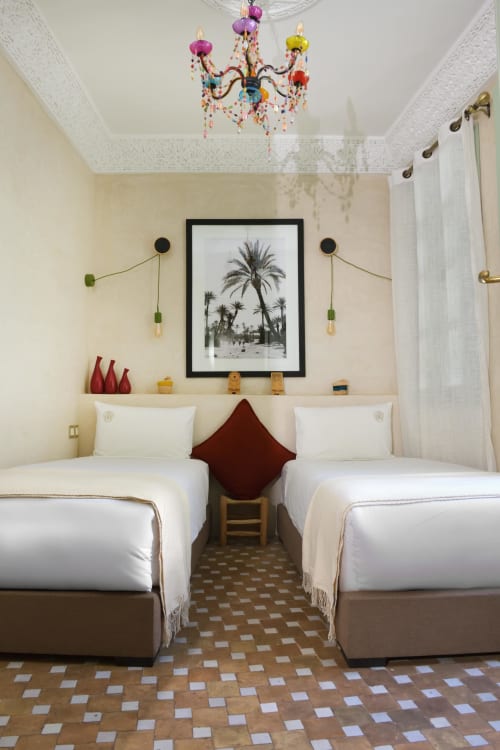Twee eenpersoonsbedden in Chambre Essaouira van Riad Palau Marrakech met kleurrijke kroonluchter en palmboomkunstwerk