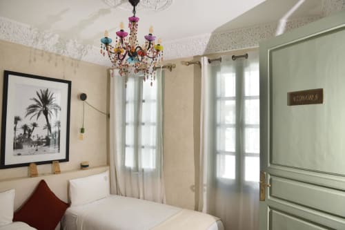 Essaouira-kamer in Riad Palau Marrakech met witte beddengoed, gekleurde kroonluchter, palmenkunst en saliegroen deuren