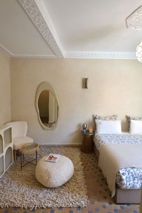 Elegant slaapkamer in Riad Palau Marrakech met beige muren, versierd plafond, ovale spiegel en comfortabel bed met decoratieve details