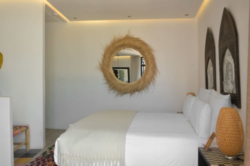 Moderne slaapkamer in Riad Palau Marrakech met ronde spiegel, wit beddengoed en Afrikaans geïnspireerde inrichting