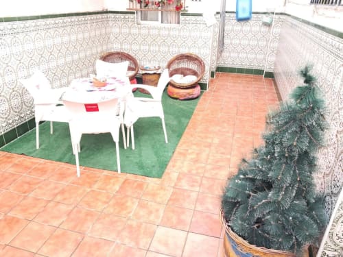 Patio de Apartamentos Tahalia en Huelva con suelo de azulejos, muebles de comedor blancos, plantas en macetas y cestas decorativas