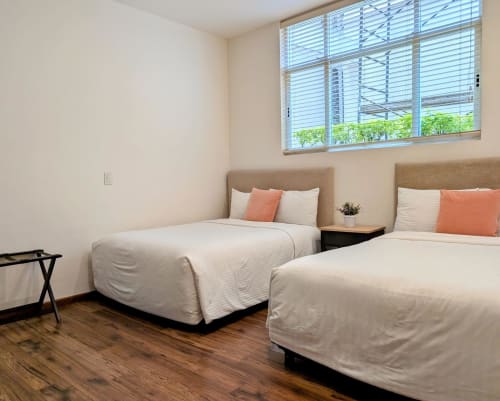 Dos camas gemelas con cabeceras beige y almohadas coral en una habitación luminosa del apartamento Casa Donceles en Ciudad de México
