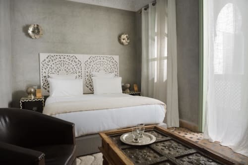 Elegante slaapkamer in Riad Palau Marrakech met sierlijk wit hoofdeinde, wit beddengoed en Marokkaanse inrichting met uitzicht op het zwembad