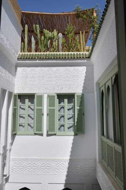 Zonnig binnenplein van Riad Palau Marrakech met witte muren, groene luiken, decoratieve tegels en potcactussen