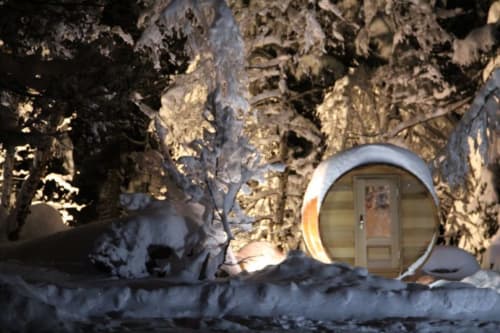 Snow-covered wine barrel entrance at Auberge Nemoz B&B in Le Haut-Bréda, France, with frosted trees and winter scenery