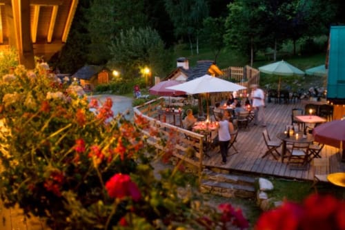 Evening gathering at Auberge Nemoz with guests under tent, wooden deck, red flowers, and ambient lighting in Le Haut-Bréda