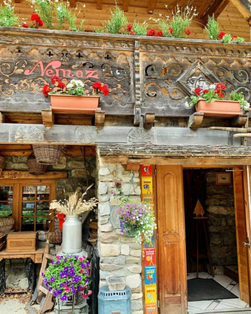 Auberge Nemoz entrance with wooden facade, red flowers, stone walls, and wooden door in Le Haut-Bréda