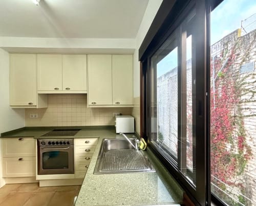 Cocina moderna en apartamento de Baiona con vistas al mar, muebles color crema, estufa y fregadero de acero inoxidable junto a ventanas