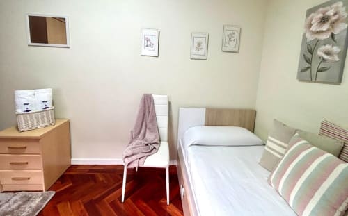 Acogedora habitación en apartamento Bitácora, Baiona con cama individual, cómoda de madera, arte floral en pared y vistas al mar