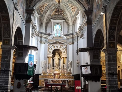 Historic church interior in Bellano, Italy with ornate altar, gothic arches, and religious statuary