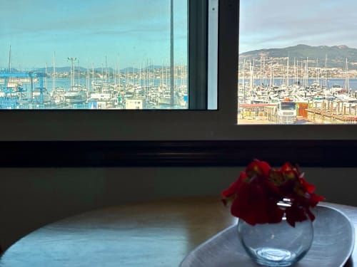 Flores rojas en jarrón sobre mesa con vistas a la Marina de Baiona, España desde el balcón del apartamento