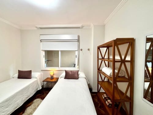 Habitación doble en apartamento Exeira, Baiona con dos camas blancas, armarios de madera, ventana con vista al mar y comodidades modernas