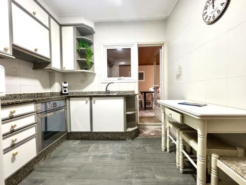Moderna cocina del apartamento de Baiona con armarios blancos, encimera de granito, electrodomésticos de acero inoxidable e isla central