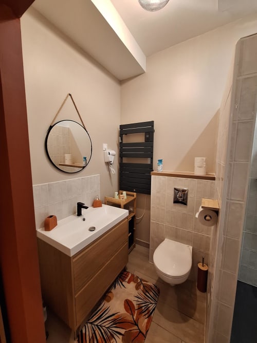 Salle de bains moderne du gîte La Cour d'Hortense avec meuble-lavabo en bois, miroir rond, porte-serviettes noir et toilettes