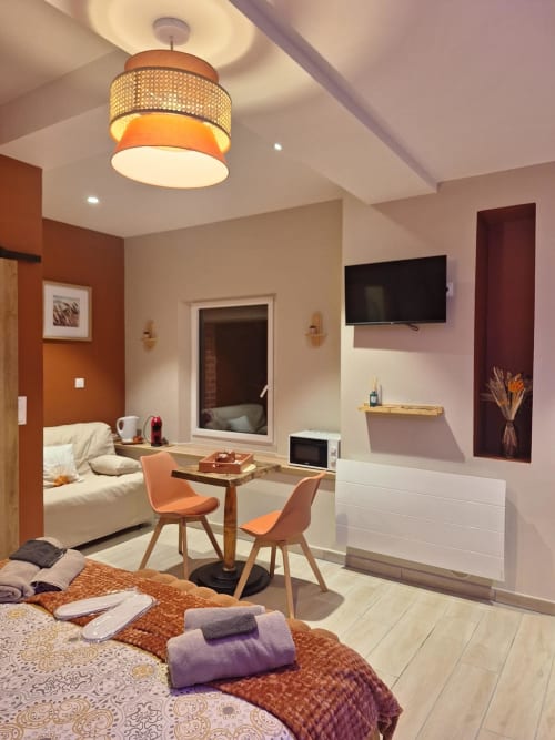 Chambre spacieuse à La Cour d'Hortense avec accents orangés, TV écran plat, coin salon et équipements modernes
