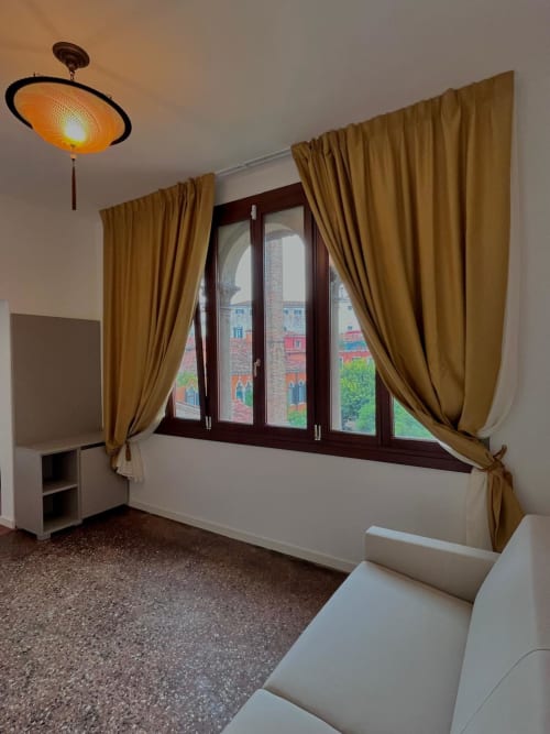 Camera Deluxe Doppia al Casanova Hideaway di Venezia con tende dorate, vista sulla città e lampada a soffitto calda
