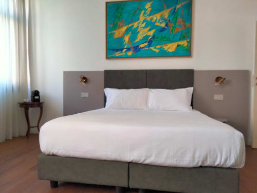 Camera moderna a Casanova Hideaway Venice con letto imbottito grigio, biancheria bianca, opera d'arte turchese e pavimentazione in legno