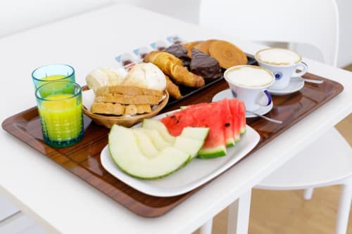 Breakfast platter at Bluemoon Sardinia featuring fresh watermelon, pastries, bread, chocolate-covered treats, and beverages