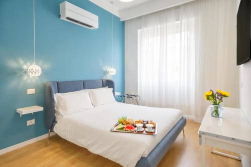 Modern bedroom at Bluemoon Sardinia in Cagliari with turquoise walls, white bedding, pendant lights, and breakfast tray
