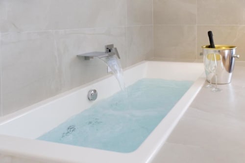 Luxurious bathtub at Bluemoon Sardinia Cagliari with running water, champagne flutes, and modern tile bathroom