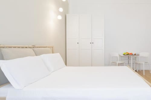 Modern bedroom at Bluemoon Sardinia in Cagliari with white bedding, wooden bed frame, wardrobe, and dining area
