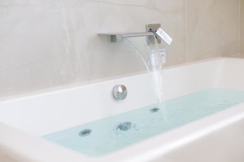 Modern chrome waterfall faucet filling a bathtub with clear water at Bluemoon Sardinia boutique hotel in Cagliari