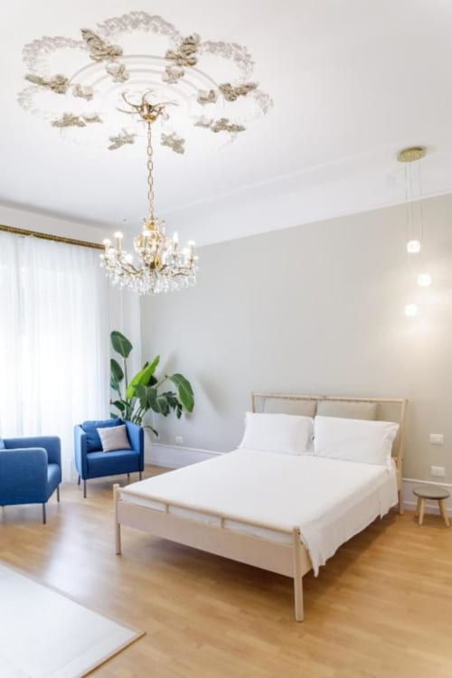 Modern bedroom at Bluemoon Sardinia in Cagliari with queen bed, crystal chandelier, blue armchair, and city view