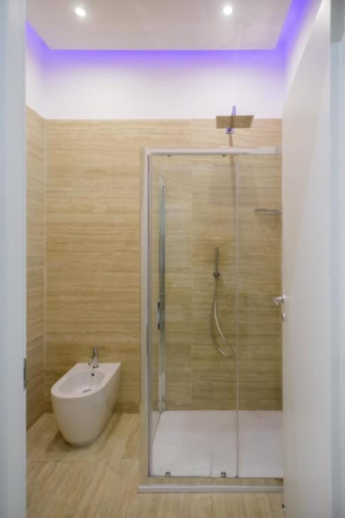 Modern bathroom at Bluemoon Sardinia in Cagliari with rainfall shower, bidet, wooden tiles, and purple ambient lighting