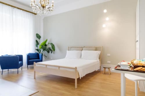 Modern hotel room at Bluemoon Sardinia in Cagliari with wooden bed, blue armchairs, plants, and city views