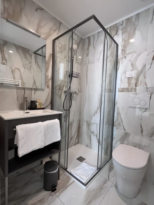 Modern bathroom at Casanova Hideaway Venice with marble walls, walk-in shower, and dark vanity sink