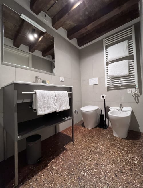 Bagno moderno a Casanova Hideaway Venice con travi in legno scuro, doccia a pioggia, scaldasalviette e cemento lucidato