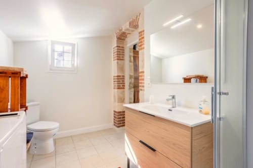 Salle de bain moderne du gîte de charme Puy du Fou avec meuble vasque en bois, lavabo blanc, toilettes et voûte en briques