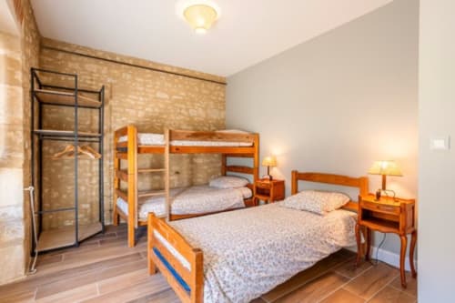 Chambre lumineuse du château de Bellevue avec lit superposé en bois, lit simple, tables de nuit, lampes, mur en briques et carrelage