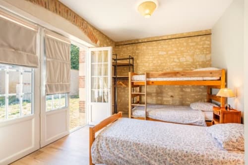 Chambre lumineuse avec lits superposés en bois, portes sur jardin et murs en briques rustiques au Château de Bellevue, Sainte-Cécile