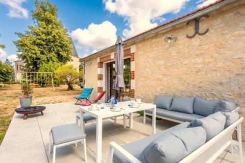 Charmante terrasse avec vue sur le jardin au Gîte de charme Puy du Fou, mobilier moderne, table de salle à manger blanche et chaumière en pierre