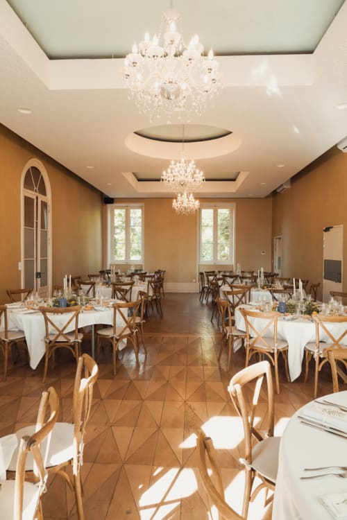 Élégante salle de banquet de La Maison Verneuil à Paray-le-Monial avec lustres en cristal, chaises en bois et tables rondes.