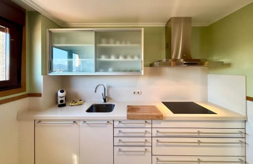 Cocina moderna con muebles blancos, estufa negra, campana acero inoxidable y vistas al mar desde ventana del apartamento Holibai