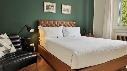 Camera doppia superior a Porta Tosa Milano con testata in pelle cognac, biancheria bianca, parete verde e vista sulla città
