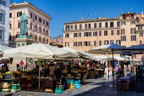 Vivace mercato all'aperto nella piazza storica di Roma con bancarelle, statua verde e edifici classici