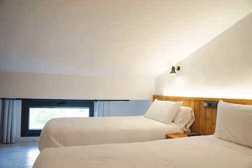 Camas gemelas limpias con sábanas blancas en una habitación luminosa con vistas a la montaña en Hostal El Ciervo, Villaciervos, con elementos de madera