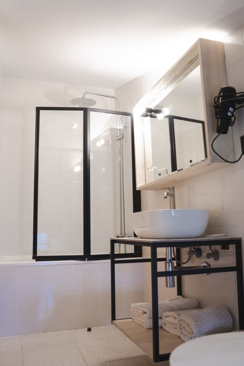 Baño moderno del Hostal El Ciervo con ducha de marco negro, lavamanos blanco, espejo y estantería para toallas.