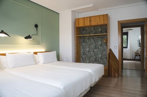Habitación moderna en Hostal El Ciervo con cama blanca, pared de acento verde, armario de madera e iluminación contemporánea