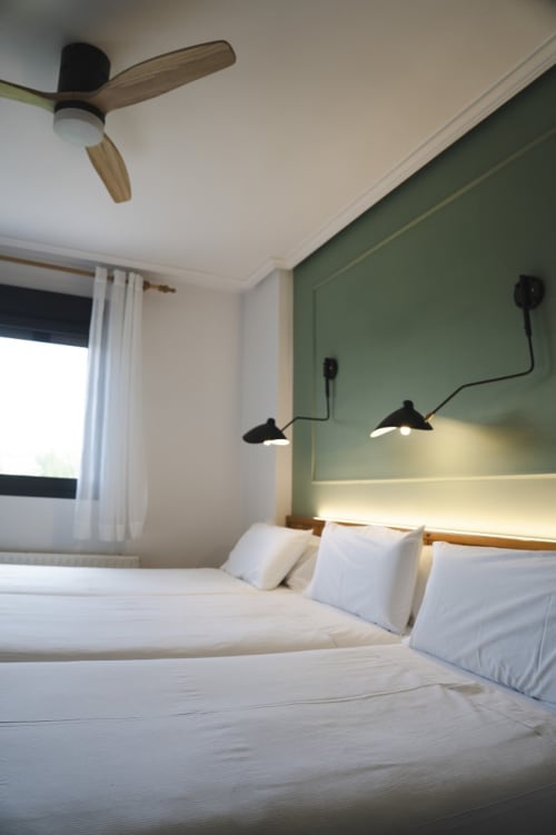 Habitación moderna en Hostal El Ciervo con ropa de cama blanca, pared de acento verde, ventilador de techo e iluminación colgante