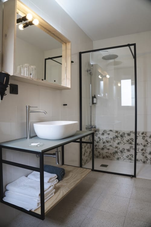 Baño moderno del Hostal El Ciervo con lavamanos tipo vasija, ducha con marco negro, espejo iluminado y toallas blancas