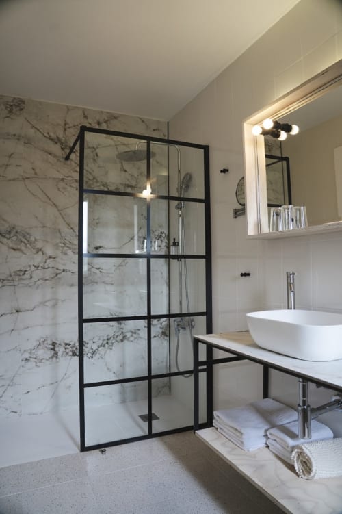 Baño moderno en Hostal El Ciervo con paredes de mármol, ducha con marco negro y lavabo de cerámica blanca