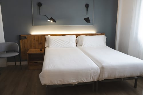 Habitación doble en Hostal El Ciervo con dos camas individuales, cabecero de madera, iluminación moderna y pared con acento azul